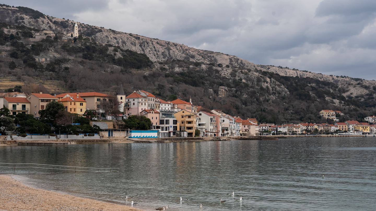 Baška na Krku izvan sezone, iza starog dijela goli krški greben