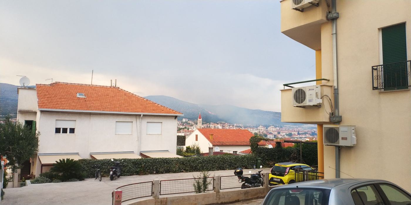 Dim i linija vatre na padini iznad obalnog grada, gledano iz stambene ulice između kuća