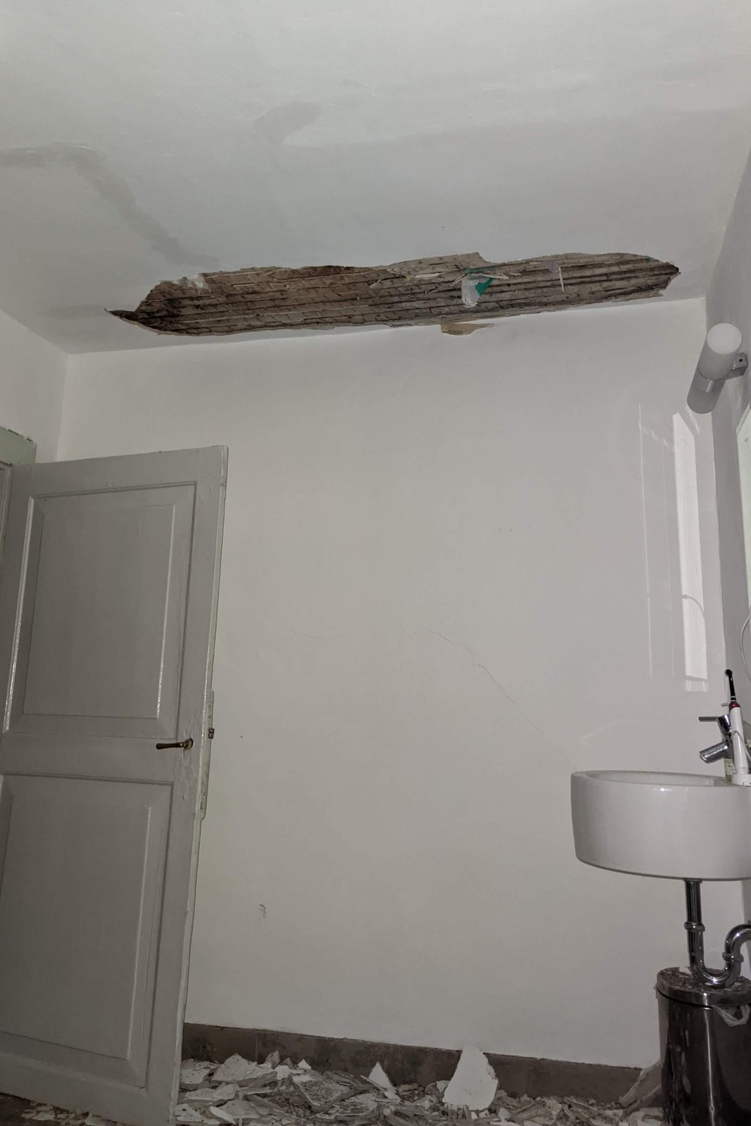 Bathroom with a long strip of ceiling plaster missing, exposing reed matting nailed to timber, plaster debris across the floor