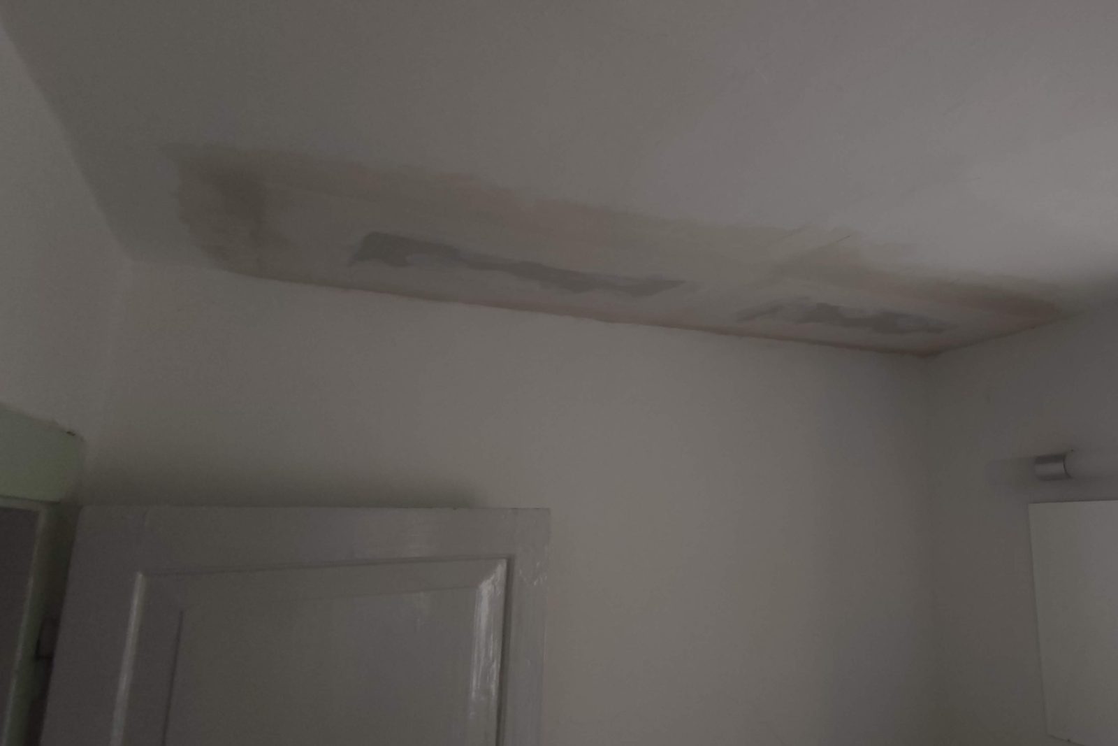 The repaired section of ceiling, freshly plastered and not yet painted, noticeably larger than the area that had originally fallen